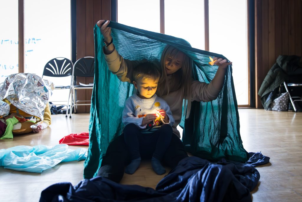 An adult and a young child play with small lamps under a translucent blue piece of fabric during a Tuneful Chatter session at The Point in Doncaster