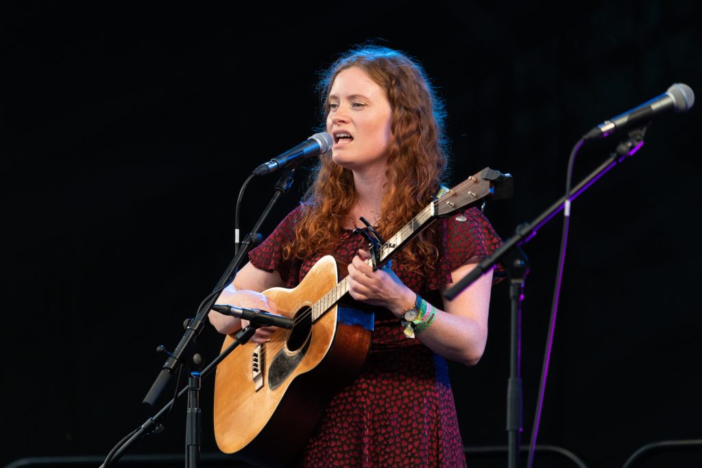 A woman sings on stage with a microphone and acoustic guitar. 