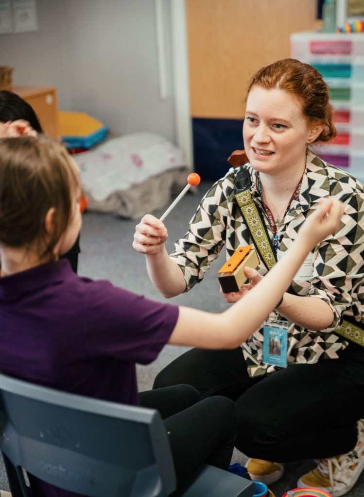 A woman teaches a young pupil how to use a percussion instrument. This is parts of a darts music programme. 