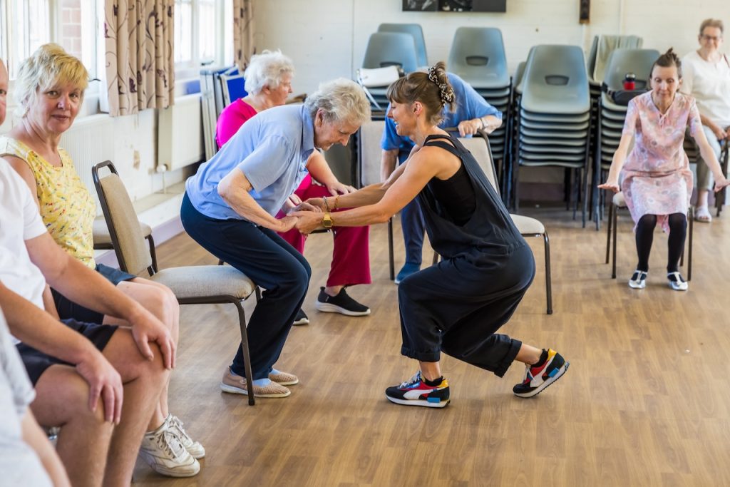 Dancer Charlotte Armitage supports a Dance On Strength and Balance participant to do some gentle movement. This is a group for falls prevention in older adults led by darts in Doncaster.