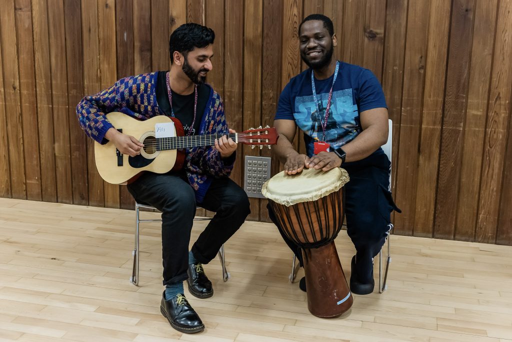 Two men sitting and playing djembe drums.